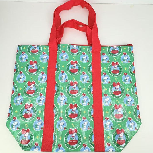 Green tote bag with red handles featuring a pattern of Peanuts Snoopy s in festive settings.